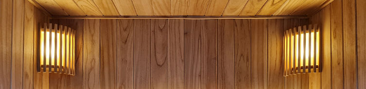 Luz de sauna colocada en la esquina superior, con pantalla de madera que difumina una iluminación cálida y suave.