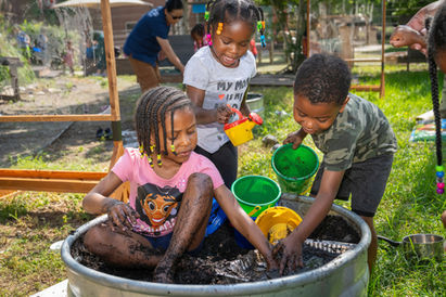 Happy children playing with dirt in an outdoor tub.