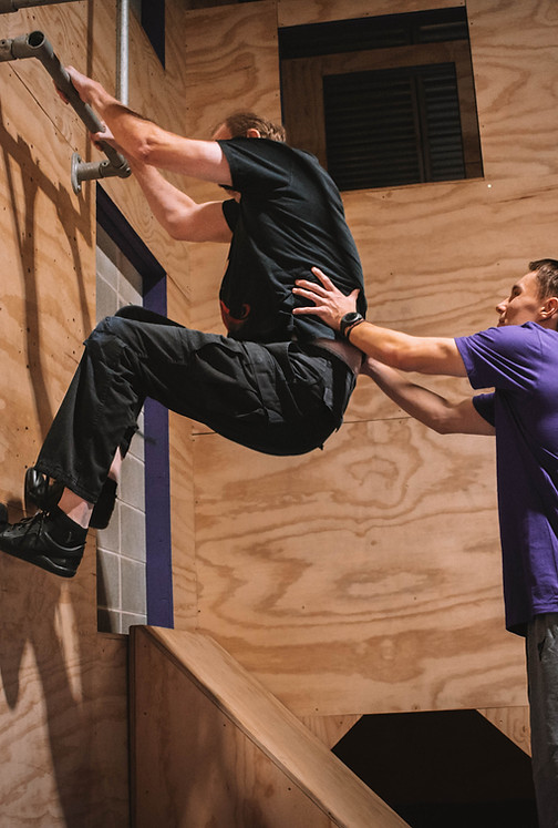 Professional coach helping adult student jump on a wall