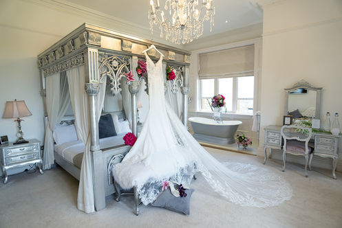 Wedding dress hanging from an ornate four-poster bed beneath a chandelier at Manor by the Lake.
