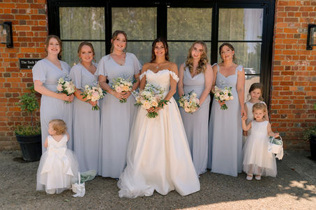 Bride with the wedding party in pale dresses holding bouquets at Lillibrooke Manor.