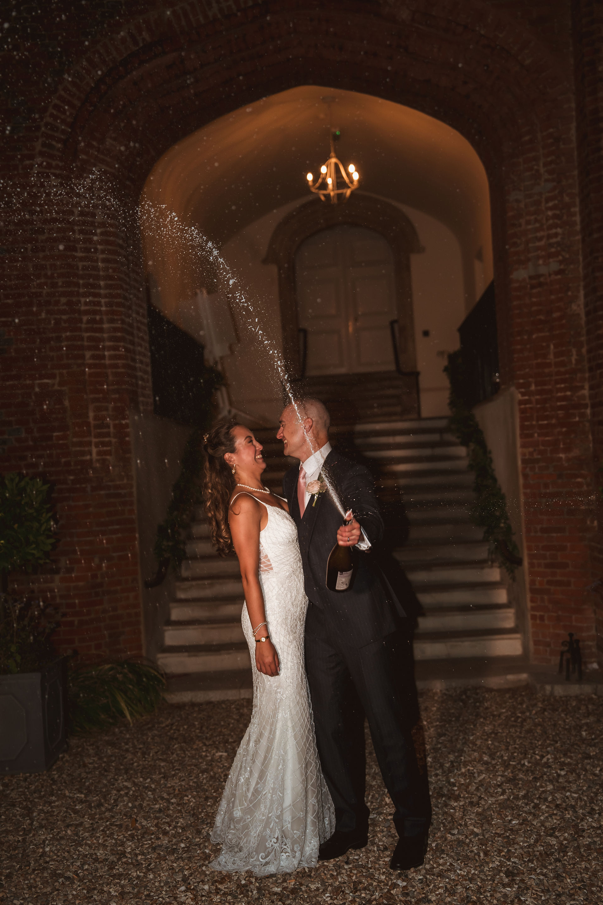 Couple spraying champagne under the lit entrance arch at night