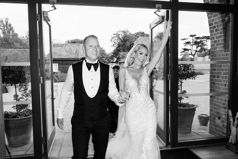 Bride raising her arm as she and the groom walk through a doorway at Wasing Estate, in black and white.