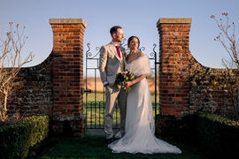 Bride and groom standing between brick gateposts at Lillibrooke Manor.