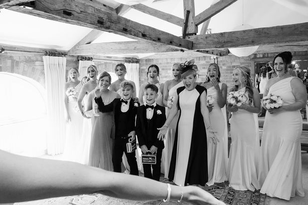 Bride posing with women and children beneath exposed beams at Wasing Estate, in black and white.