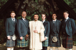 Groom in a cream embroidered jacket with men in tartan kilts at Bury Court Barn.