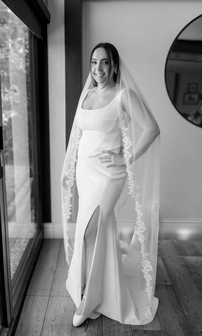 Bride in her wedding dress and lace-edged veil beside a window at Silchester Farm, in black and white.