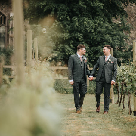 Two grooms smiling together during relaxed outdoor wedding portraits in East Anglia