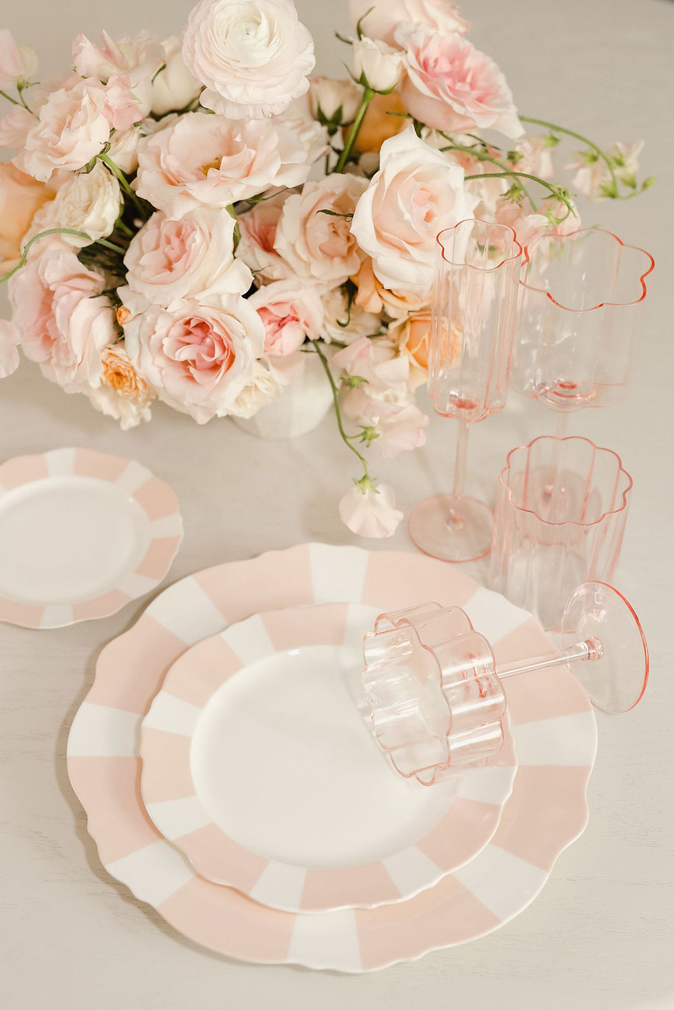 Blush pink dinnerware styled with florals, ideal for luxury wedding tablescapes and premium event rentals.