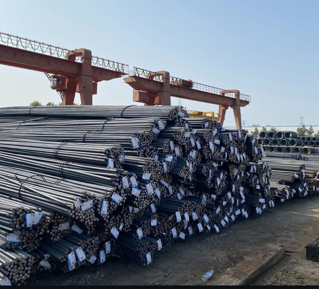 Stacks of steel rebar in a yard with cranes