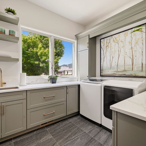 Custom laundry room featuring celadon green cabinetry, quartz countertops, brass hardware, open shelving, utility sink, and built-in storage with mountain views.