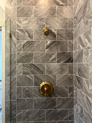 A shower with gold fixtures and gray tiled walls in a bathroom setting.