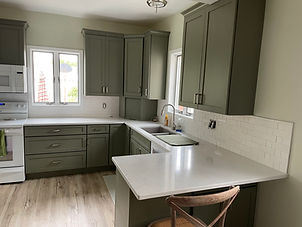 Modern kitchen with green cabinets, white countertops, and a wooden chair.