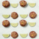 Rows of chocolate pastries with hazelnuts, alternating with lime wedges on a light green background, creating a colorful pattern.