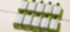 Ten green bottles labeled "ACIDE" arranged in a grid on a beige surface, casting soft shadows.