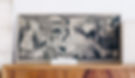 Monochrome artwork on a wooden shelf features abstract, chaotic figures with intense expressions, set against a plain white wall.