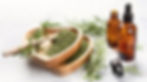 Wooden bowls with dried herbs and a spoon, rosemary sprigs, and amber dropper bottles on a light surface. Fresh, natural vibe.