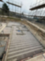 Construction site with scaffolding surrounding a foundation of concrete blocks. Overcast sky, dirt, and trees in the background create a serene mood.