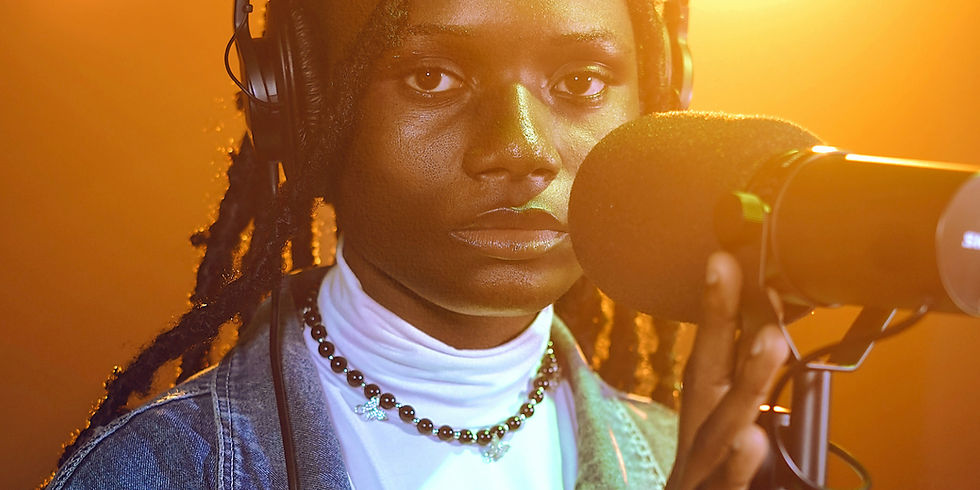 Independent artist wearing headphones records vocals into a studio microphone under warm orange lighting.