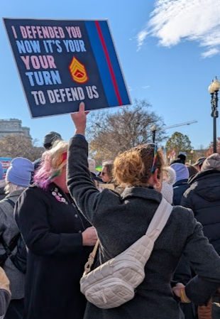Military Veteran supporting transgender health care carrying a sign that says, "I defended you. Now it's your turn to defend us."