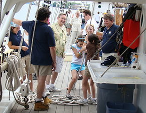 two little girls laughing while pulling on ropes and their dad and a crew member stands nearby on the gazela
