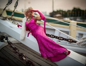 a woman dressed in a pink 1920's sparkly dress sitting on the bow of the gazela