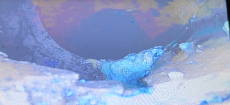 Close-up of a corroded, blue-tinged pipe with rust spots, against a blurred background. The mood is deteriorated and aged.