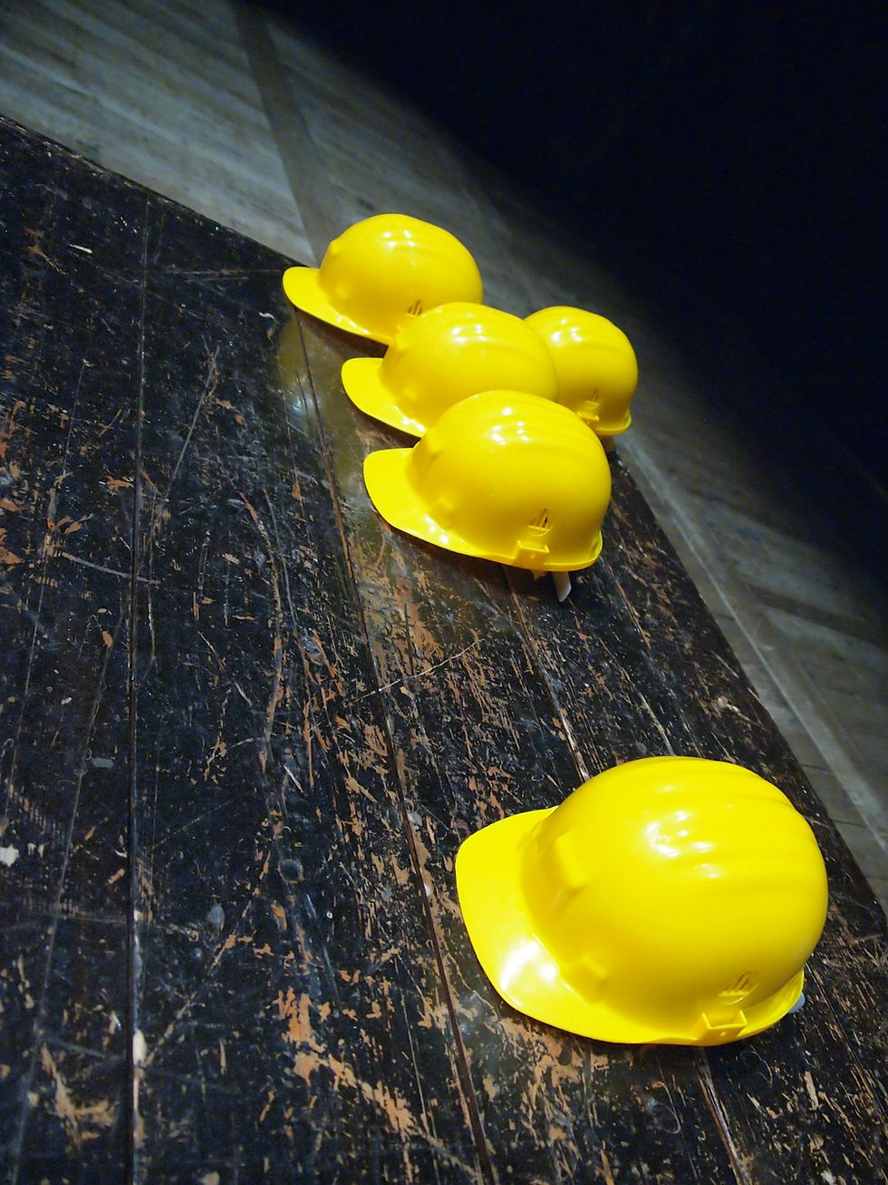 Five yellow hard hats are lined up on a worn, dark wooden surface. The setting appears industrial and dimly lit, with a focused, orderly mood.