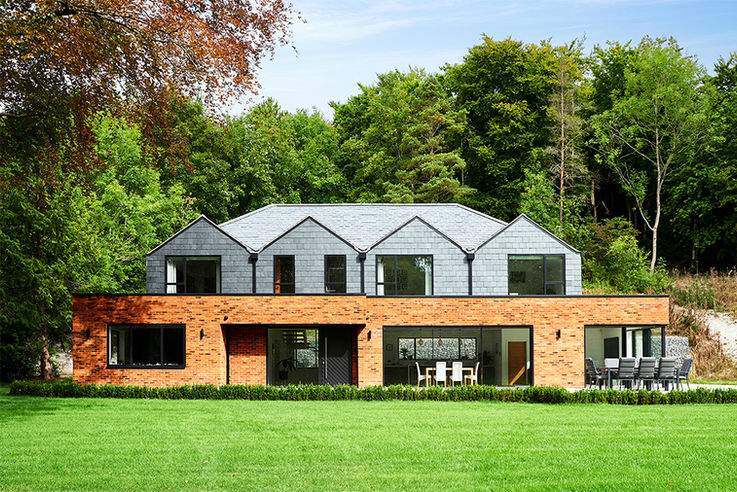 Luxury home new build in Surrey, the photograph shows the exterior of the building and its unique shape, with a cloudy blue sky. By architectural photographer James Morris, Sussex based