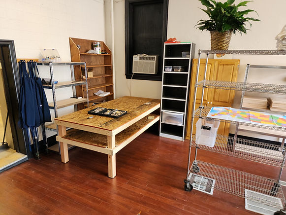 The corner of a pottery studio including tables, shelves, and cabinets.