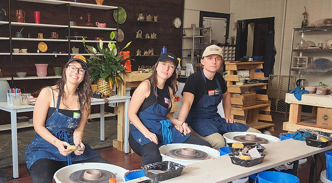 A group of three people pose as they work on the pottery wheel.
