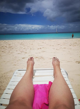 Feet propped up on a pristine white-sand beach, with turquoise water in the distance