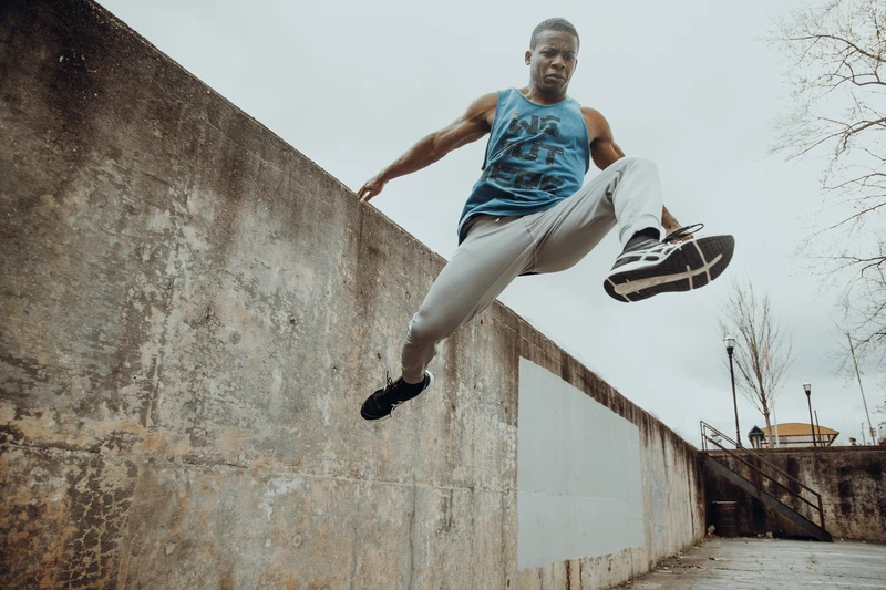 Black parkour athlete performing tic tac off of a concrete wall wearing a tanktop in a parking lot