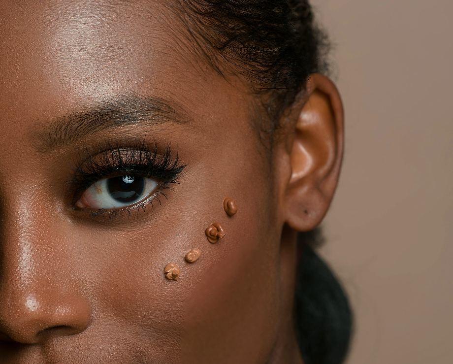 Extreme close-up of dark-skinned person's eye, with makeup droplets along cheekbone.