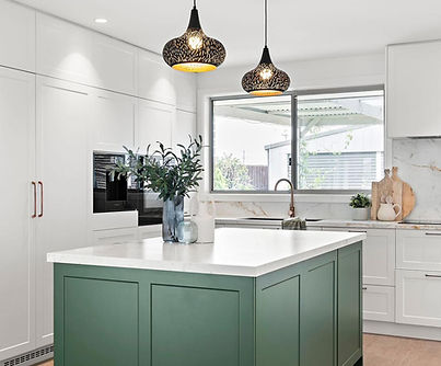 Angle view of a contemporary renovated kitchen showing a green island, marble-look benchtops, black patterned pendant lights, and built-in appliances.