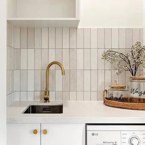 Laundry renovation with undermount sink, stone benchtop, vertical tile splashback and brass tapware