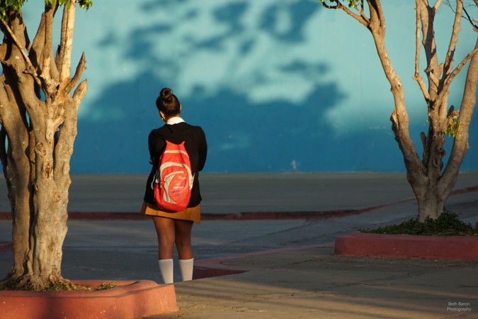 A girl waits impatiently in the early morning sunshine outside a school. Trinidad, Cuba