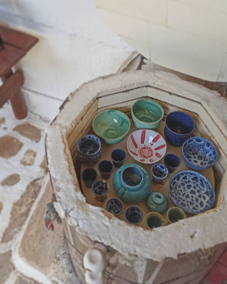 Freshly glazed ceramic bowls and cups inside a pottery kiln after firing, featuring blue, green, and red designs.