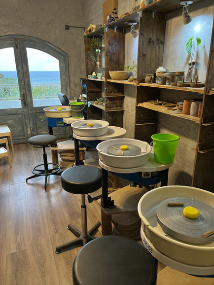 Pottery studio in Crete with wheels set up for a workshop, overlooking the sea through open double doors.