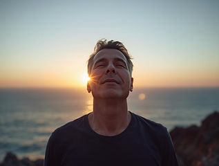 Ein Mann schaut entspannt und ruhig mit geschlossenen Augen aufs Meer im Sonnenuntergang.J