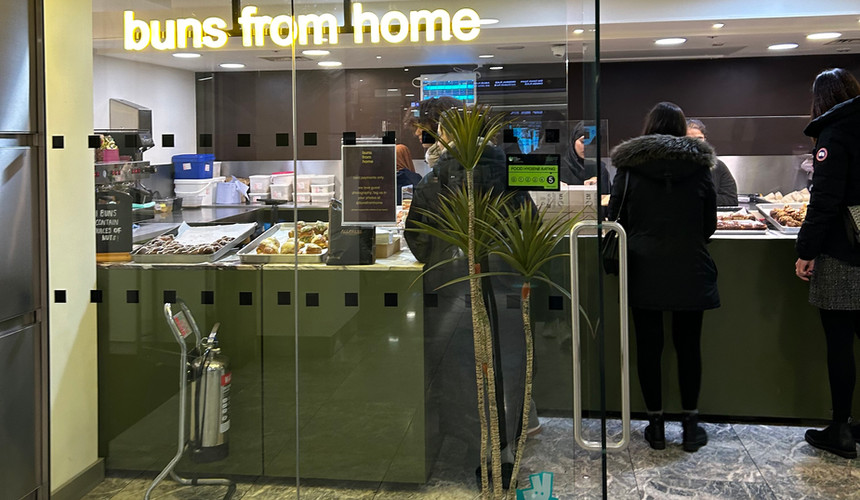 Glass doors with a neon sign saying buns from home with people inside buying pastries