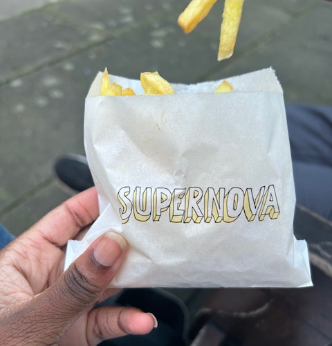 A hand holding a bag of chips in a white bag with yellow and black writing that says supernova