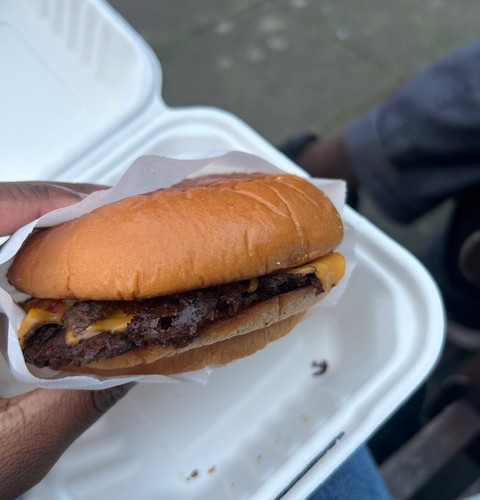A hand holding a cheeseburger over a disposable plastic white food box