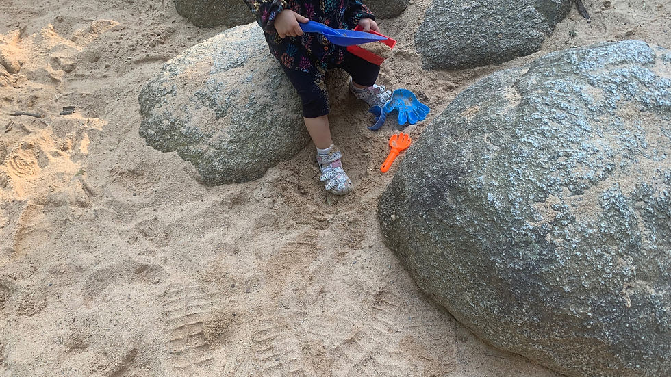 Kind mit Sandförmchen, sitzt auf Steinen im Sandkasten