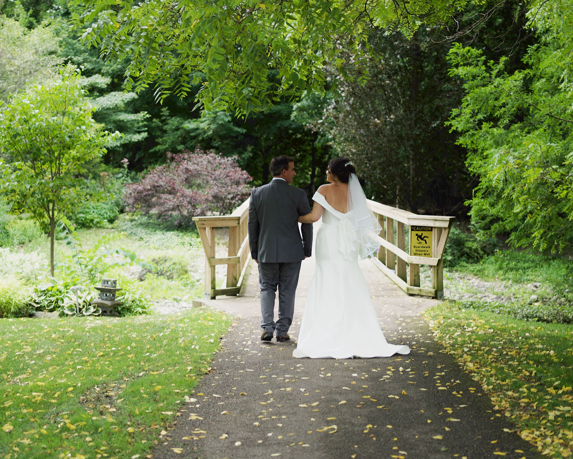 Bride and groom walking hand in hand toward the arched bridge at Civic Garden Complex in summer
