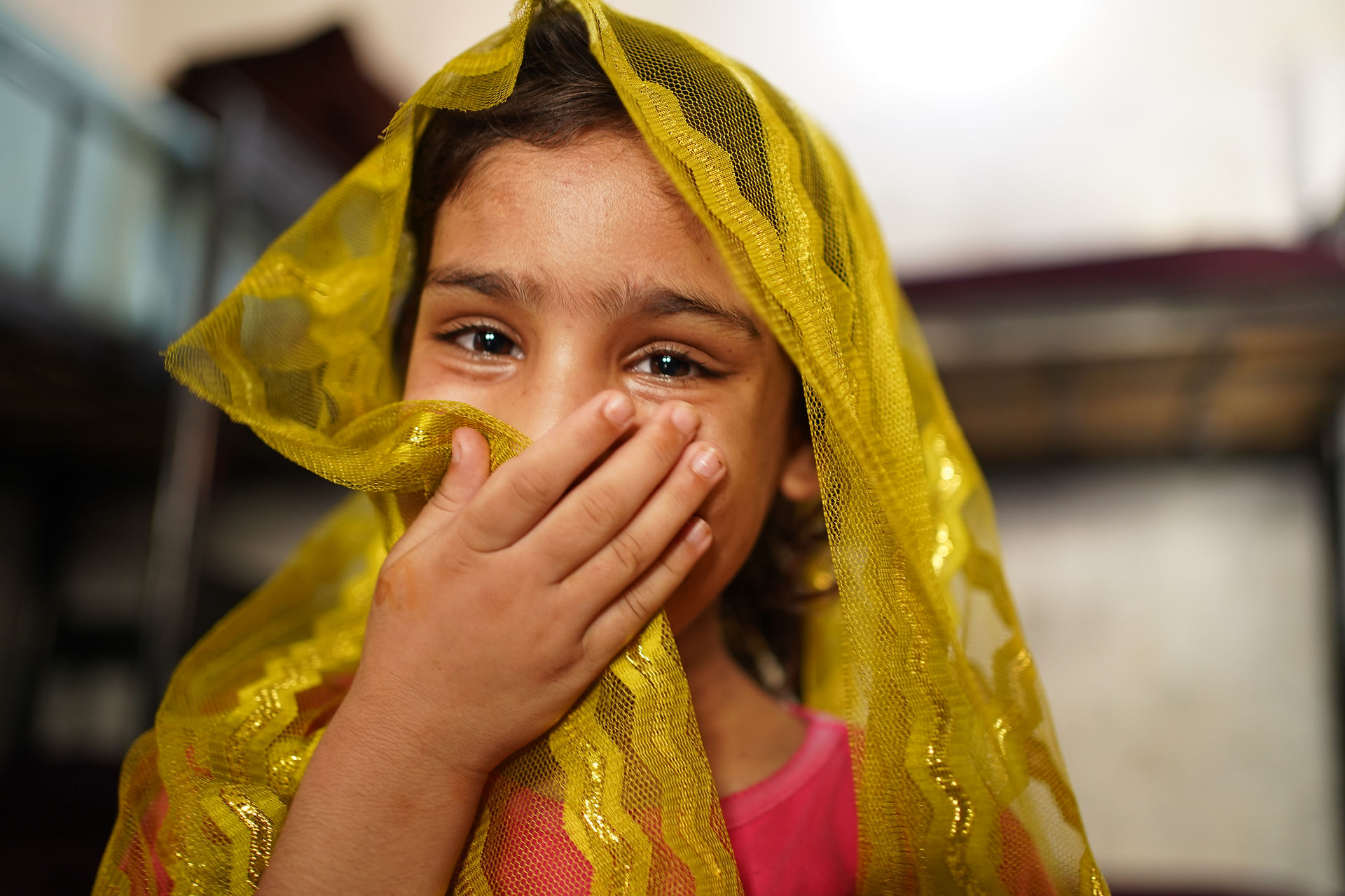 Young girl giggling and camera-shy during a photoshoot for a non-profit NGO in Pakistan, candid joyful moment