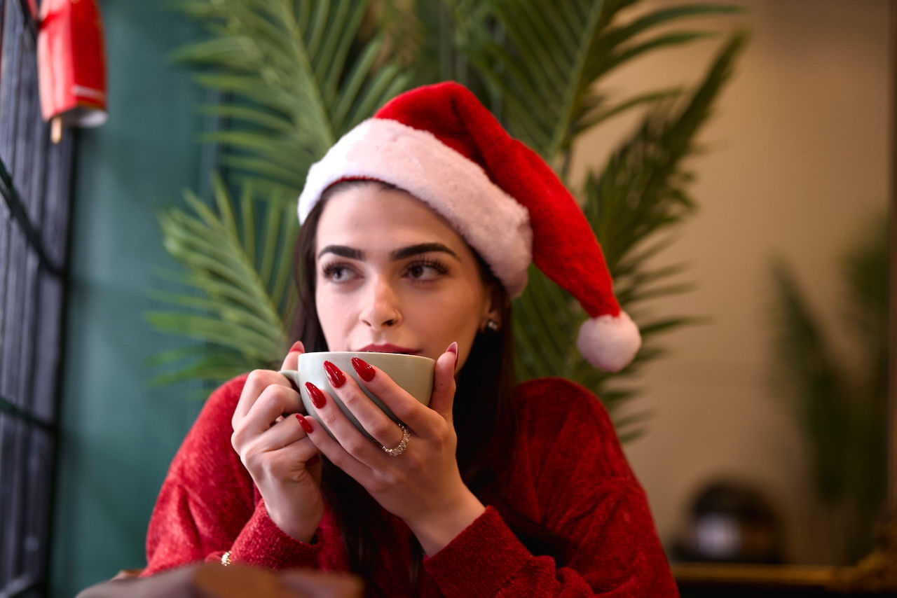enjoying her coffee portrait of a woman wearing a red sweater and Santa hat inside a cozy Christmas café in downtown London Ontario