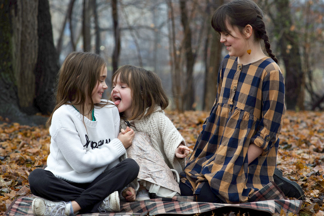 Siblings enjoying winter, sitting together on damp grass and being themselves at Old South Park in London, Ontario, candid outdoor moment