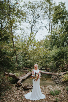 A bride stands in the middle of north nolan creek in the very back of the property at Hidden Creek at Stonehaus with her bridal bouquet.
