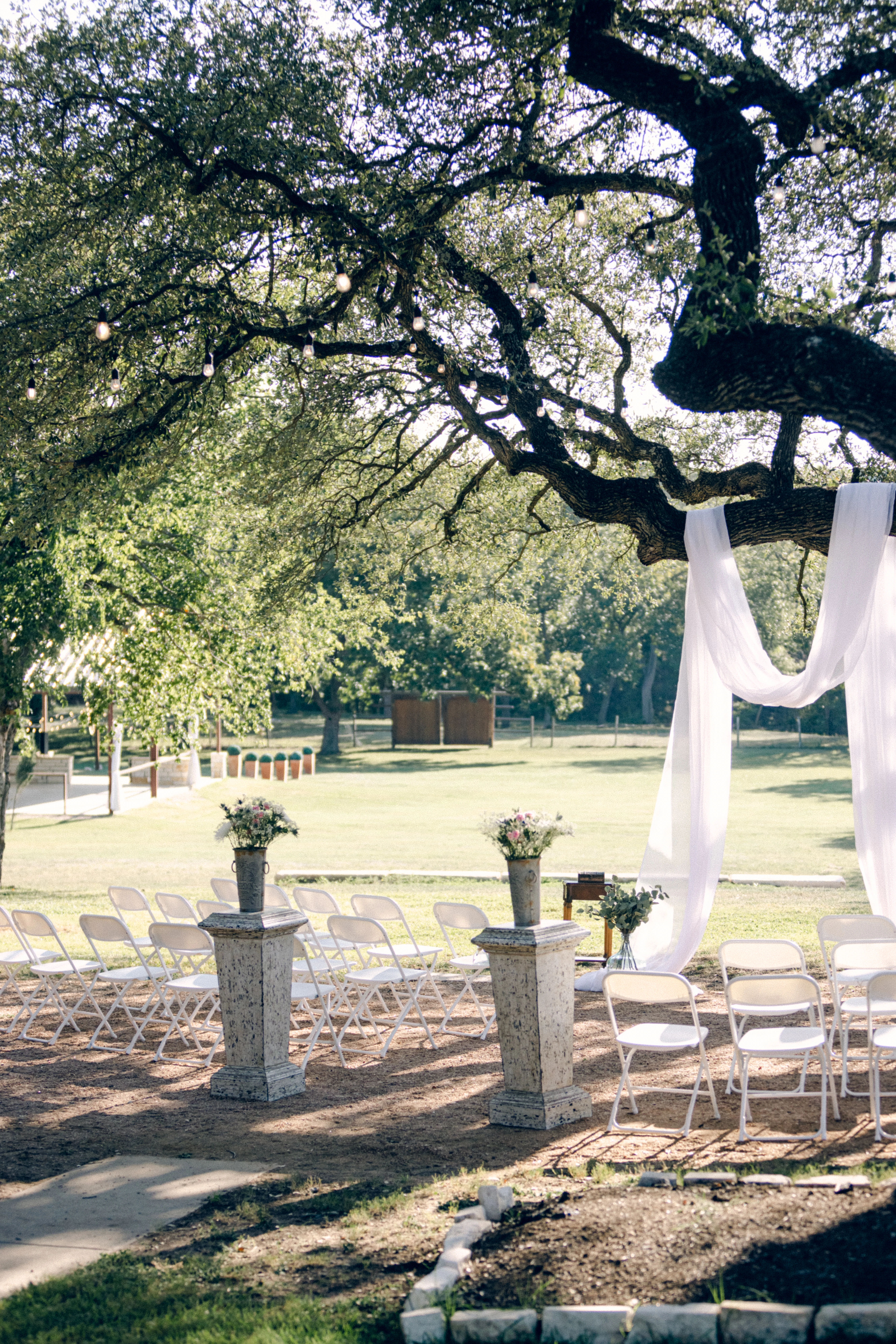 a verticle shot of hidden creek's ceremony site under the oak trees. The tree is drapped with a white drape and flank by two pillers